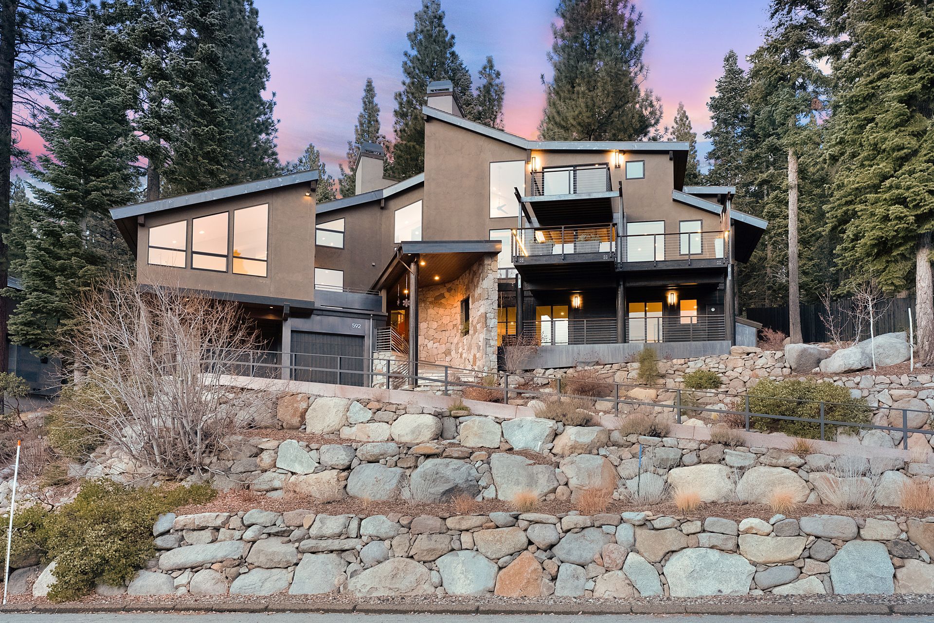 A large house is sitting on top of a rocky hill surrounded by trees.