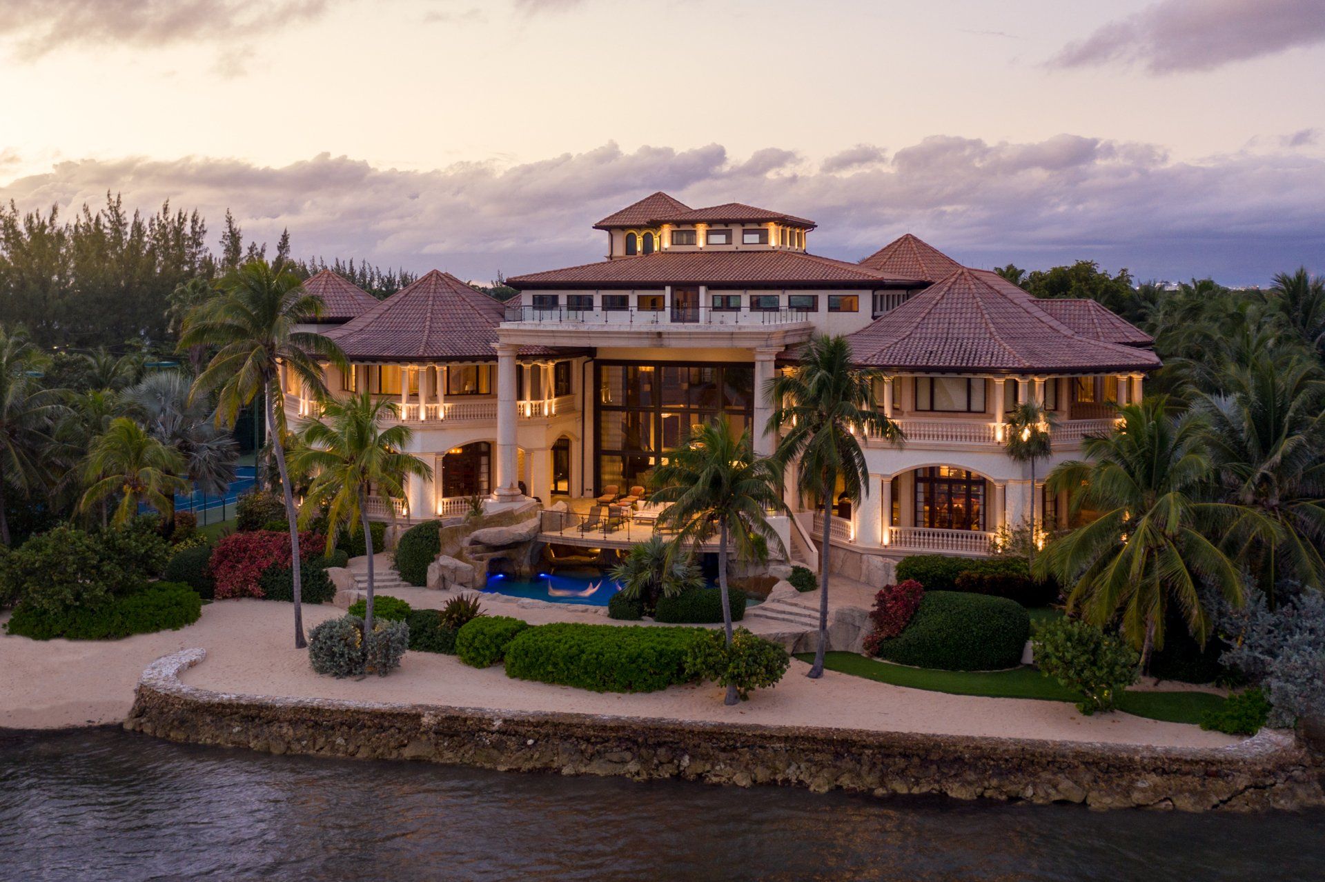 an aerial view of a large house surrounded by palm trees next to a body of water