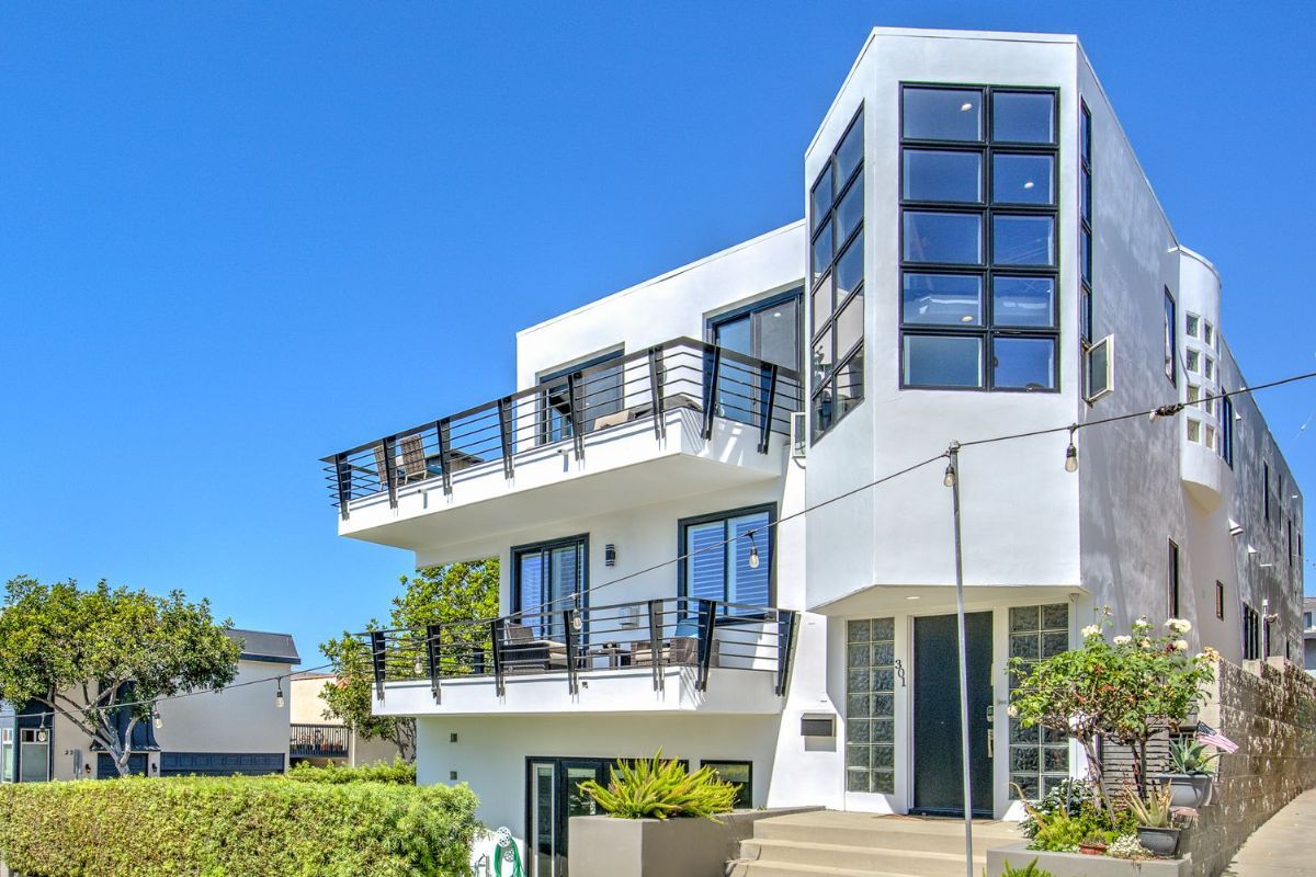 A large white house with a balcony and stairs on a sunny day.